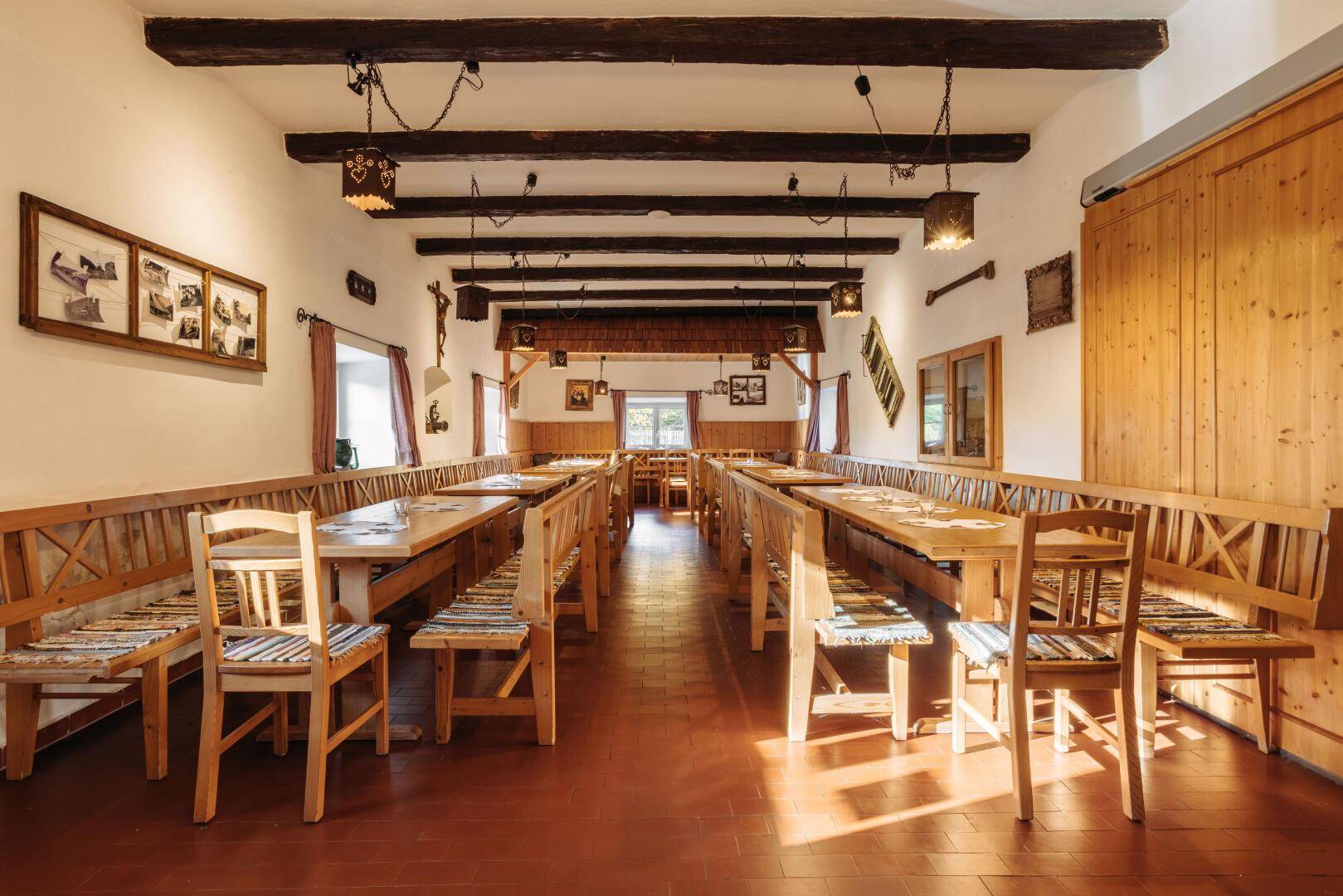 Großer Speisesaal mit Holzbänken, Tischen und sichtbaren Deckenbalken in traditionellem Stil.