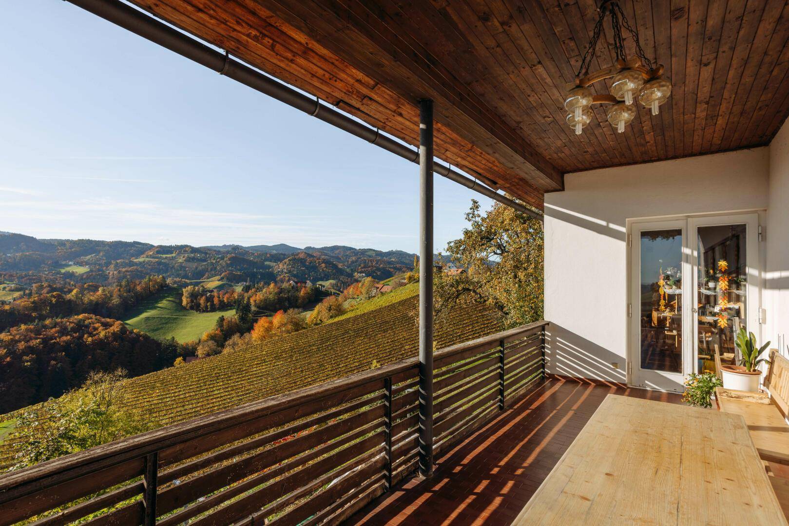 Überdachte Loggia mit Holztisch und weitem Blick über die herbstlichen Weinberge.