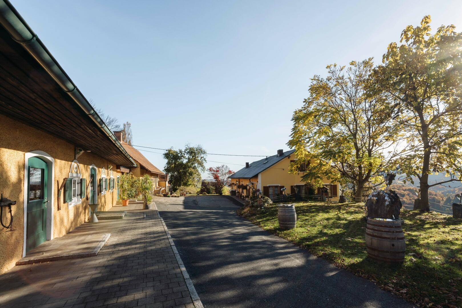 Gelbes Gebäude mit gepflastertem Weg und Bäumen, die Schatten auf die Einfahrt werfen.