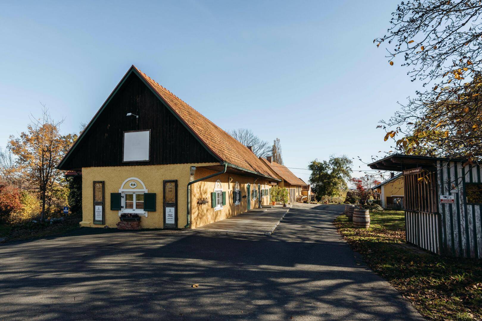 Traditionelles gelbes Gebäude mit rotem Ziegeldach und grünen Fensterläden in ländlicher Umgebung.