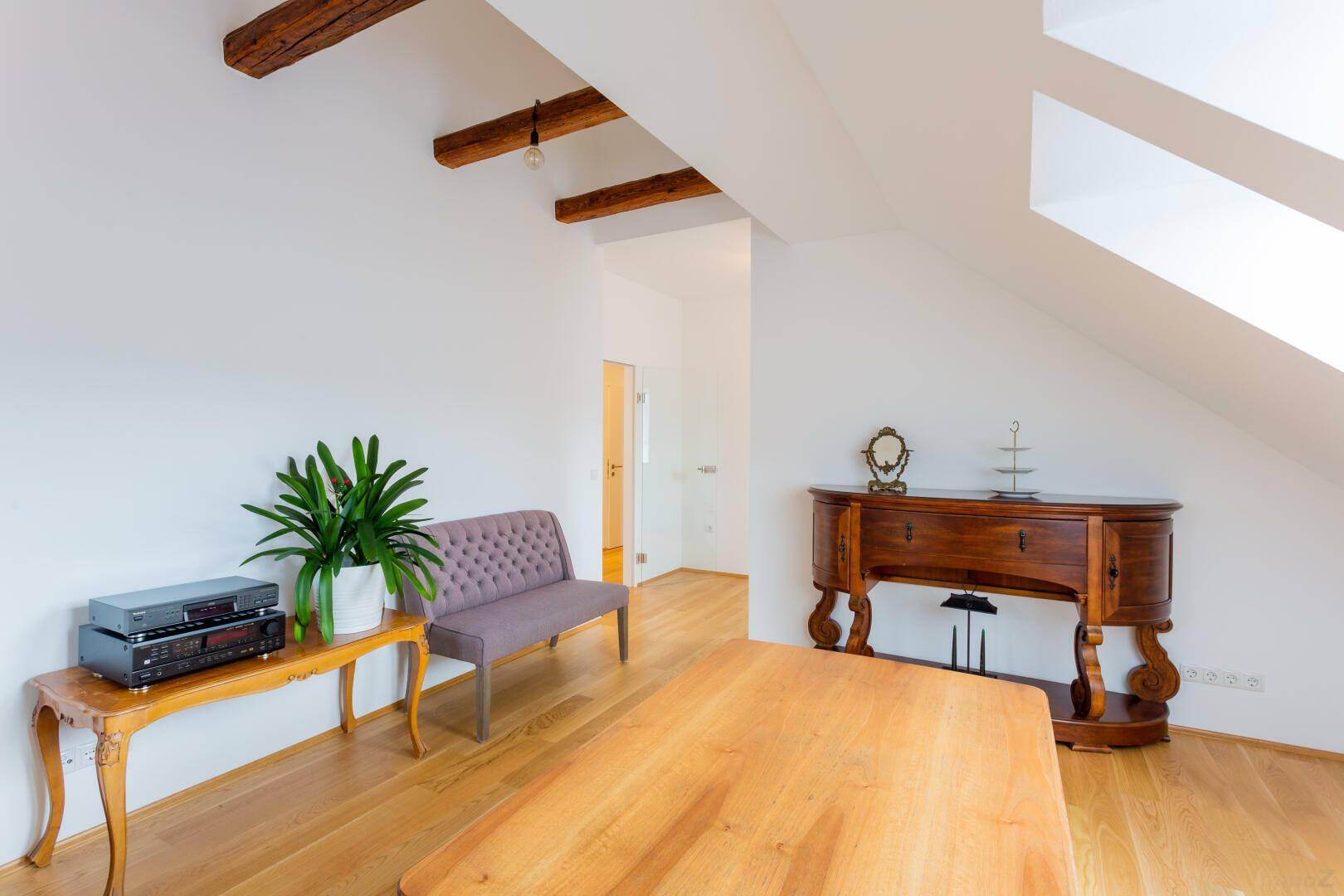 Geräumiger Wohnbereich mit Holzbalken, Parkettboden und klassischem Mobiliar im Dachgeschoss.
