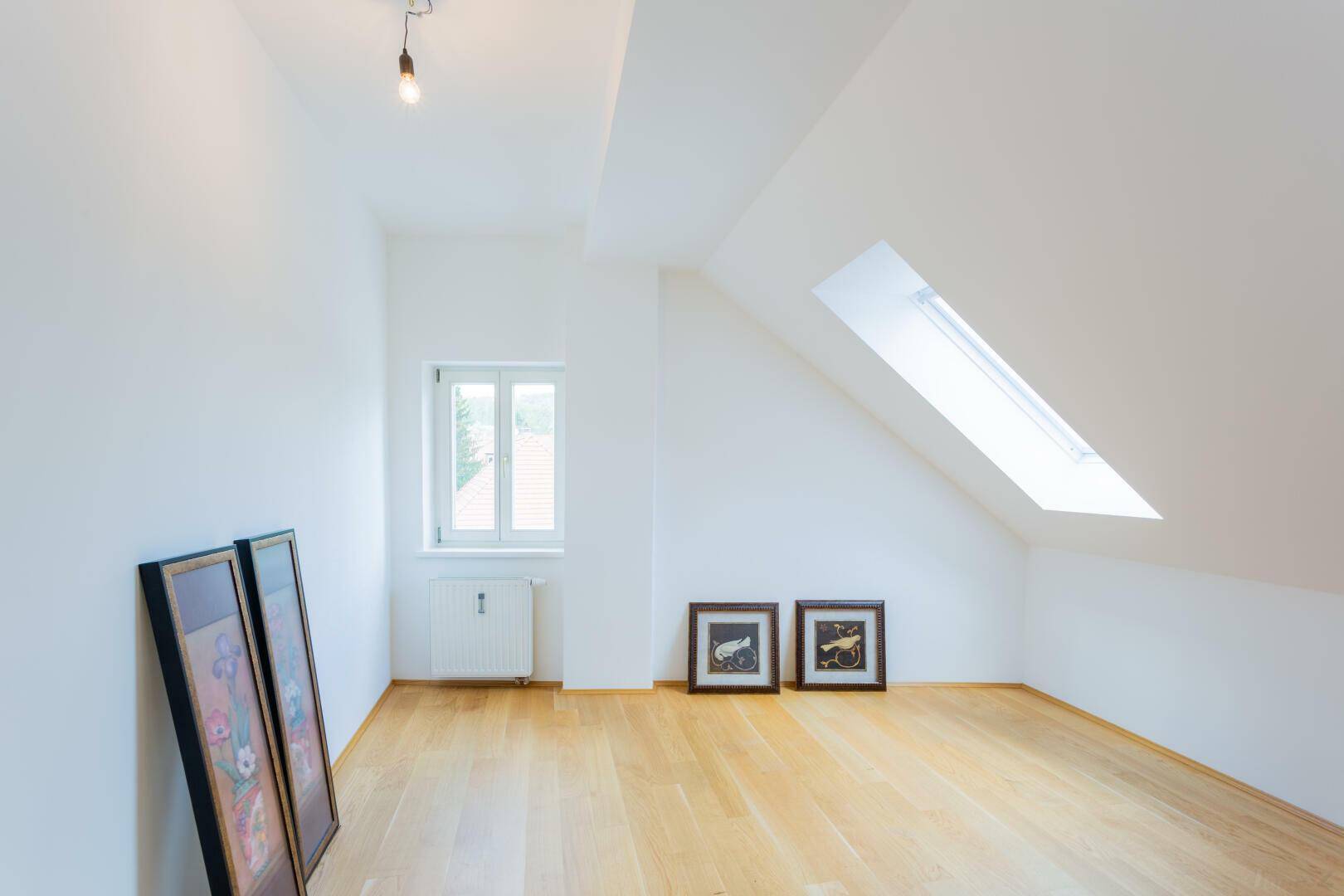 Leerer Raum im Dachgeschoss mit Dachfenster, normalem Fenster und hellem Parkettboden.