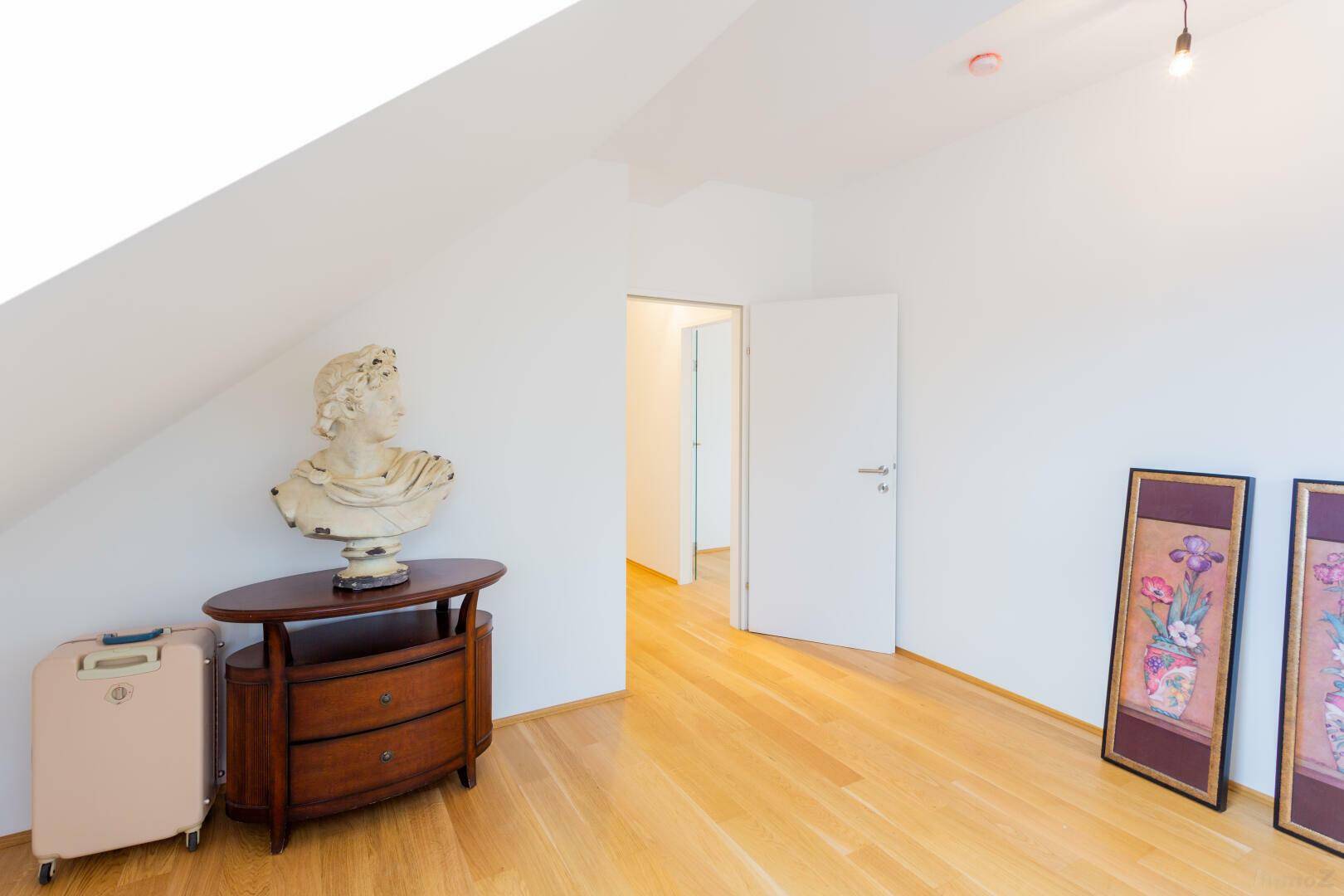 Heller Raum im Dachgeschoss mit Parkettboden und Zugang zu weiteren Zimmern.