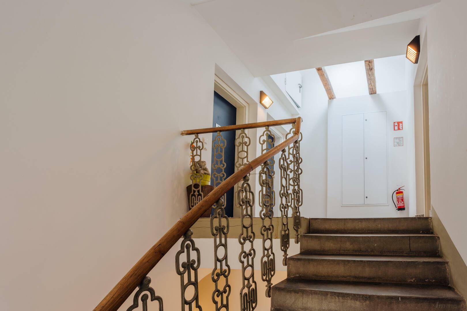 Historisches Treppenhaus mit schmiedeeisernem Geländer und sichtbaren Holzbalken.