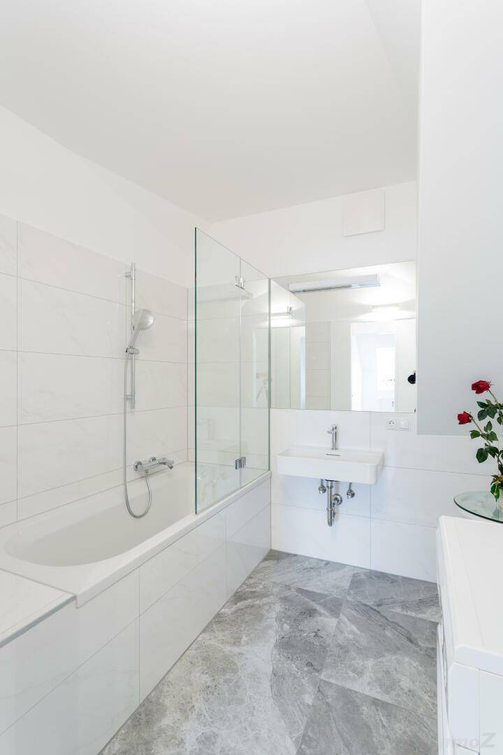 Modernes Badezimmer mit Badewanne, Duschwand, Einzelwaschbecken und grauen Fliesen.