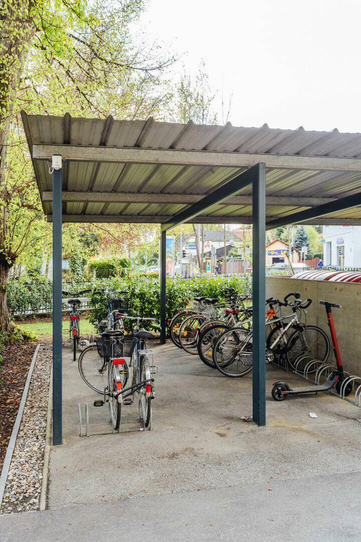 Überdachter Fahrradabstellplatz mit mehreren Fahrrädern und einem Roller.