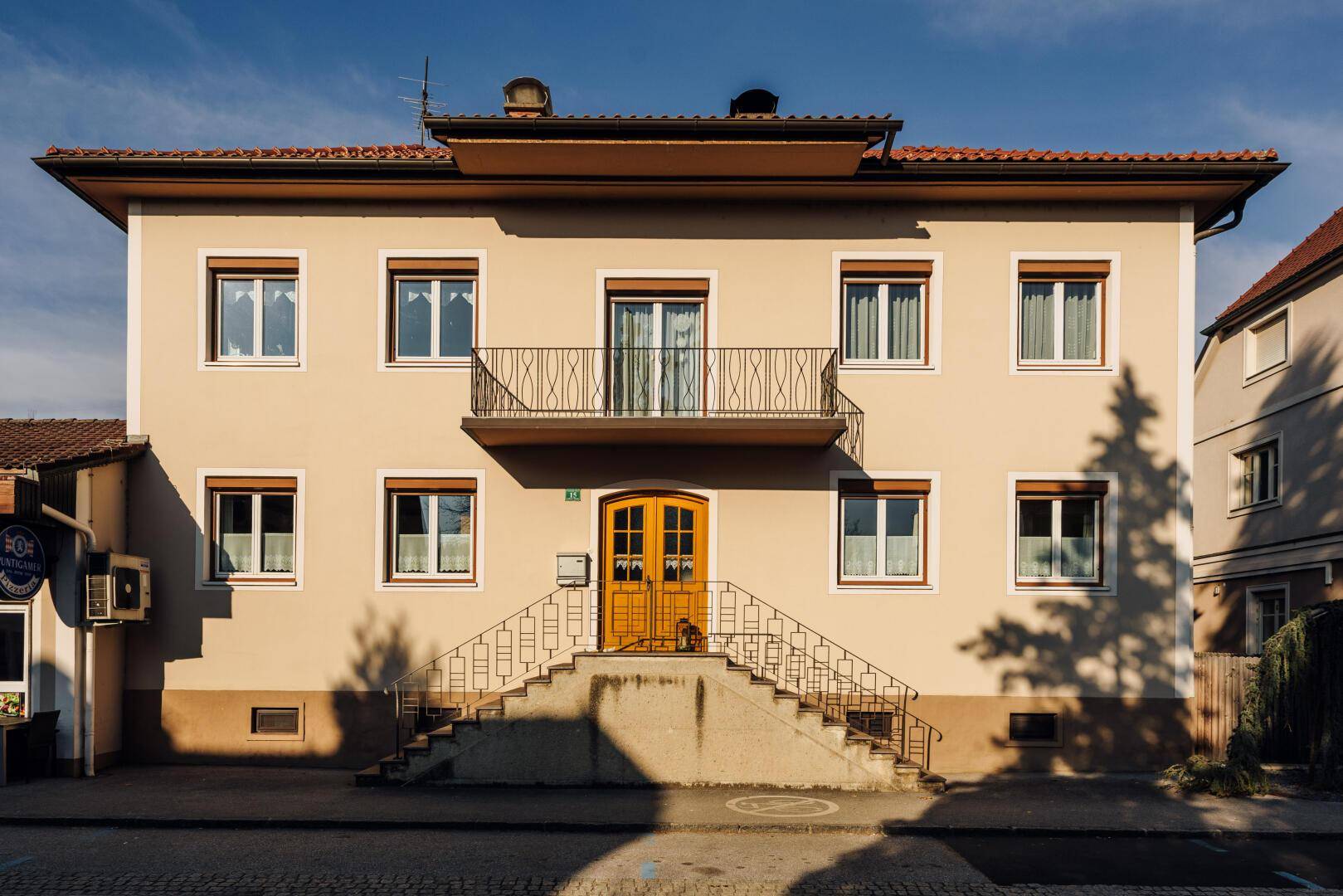 Traditionelles Mehrfamilienhaus mit Balkon, Außentreppe und gelber Fassade.