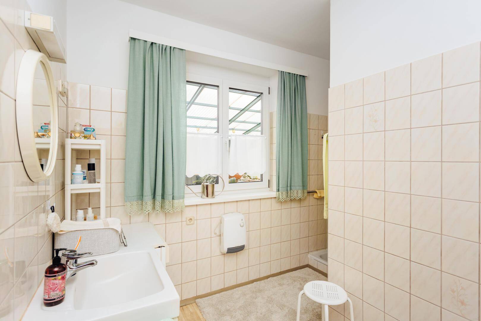 Badezimmer mit Waschbecken, Spiegel und beigen Fliesen.