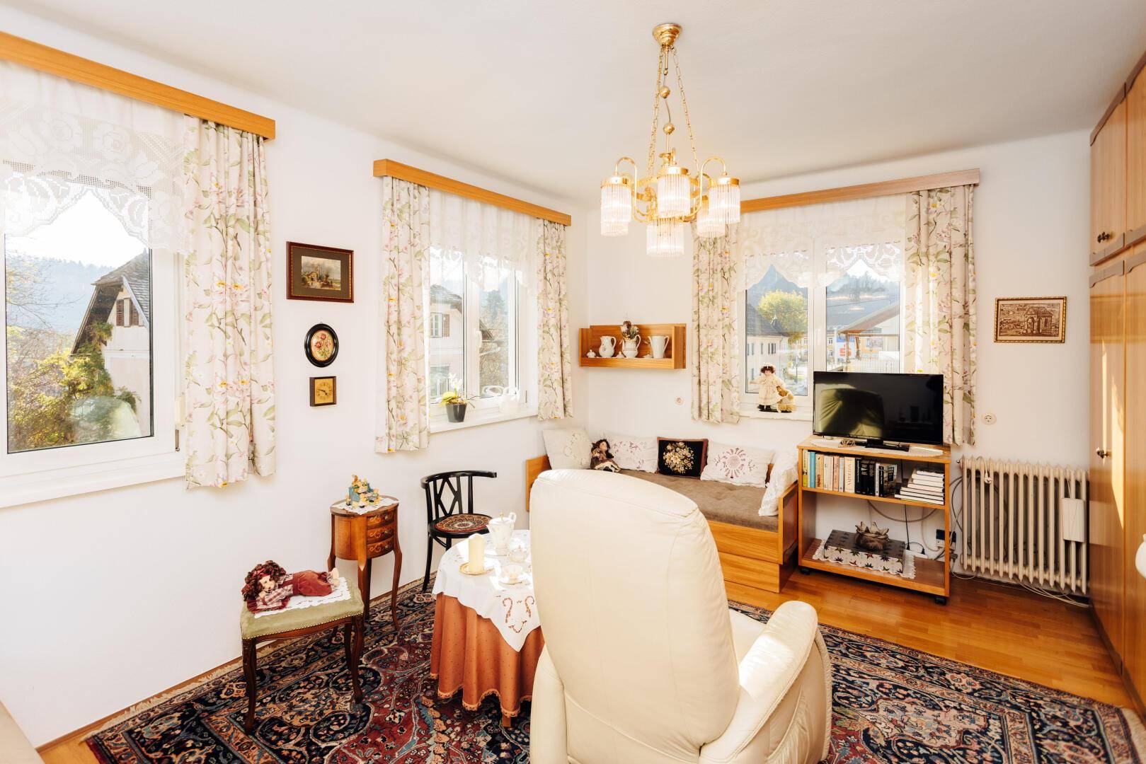 Gemütliches Wohnzimmer mit mehreren Fenstern, Teppich und traditionellen Möbeln.