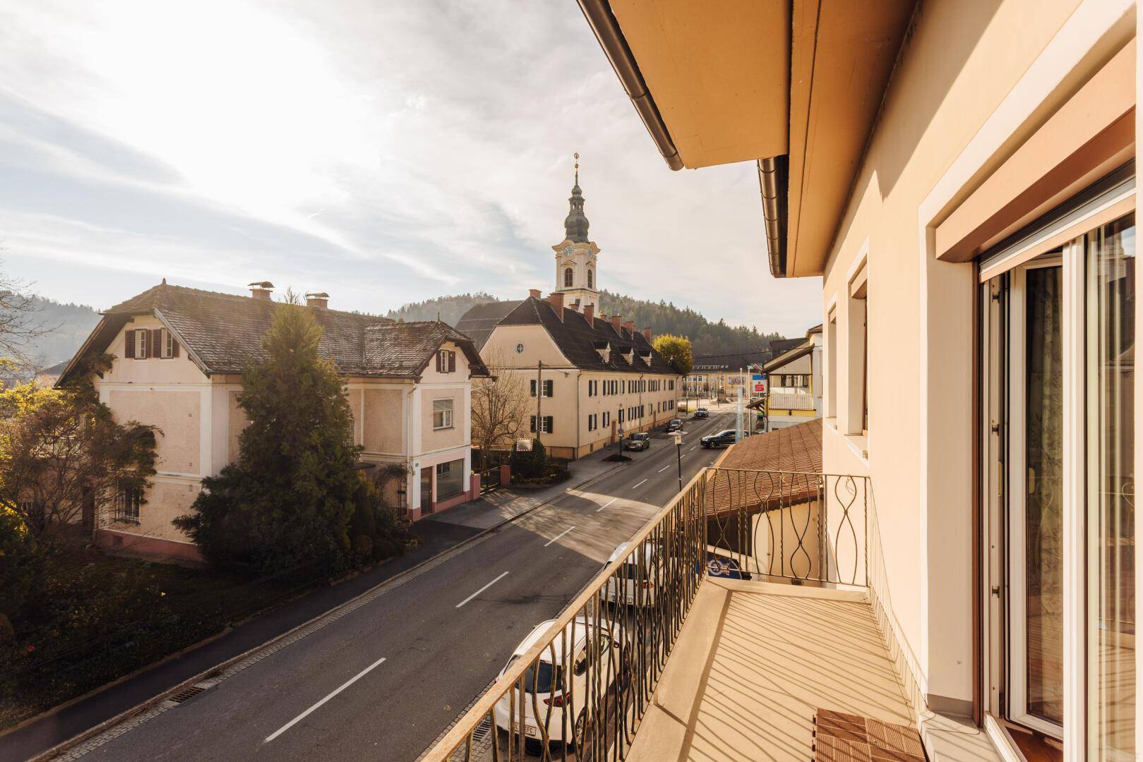 Balkon mit Blick auf die Straße, umliegende Häuser und einen Kirchturm.