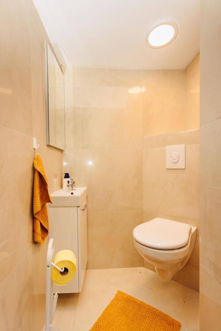 Helles Gäste-WC mit beigen Fliesen und Spiegelschrank.