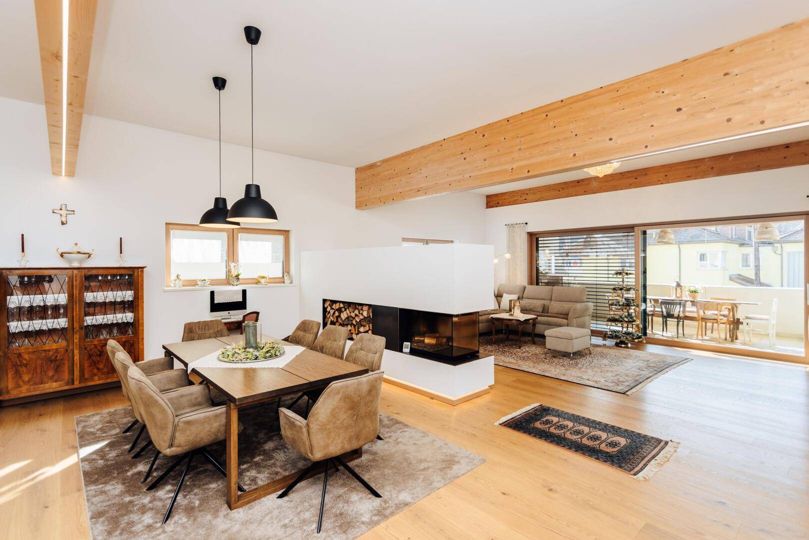 Geräumiger Wohn-Essbereich mit Holzbalken, Kamin und Zugang zum Balkon.