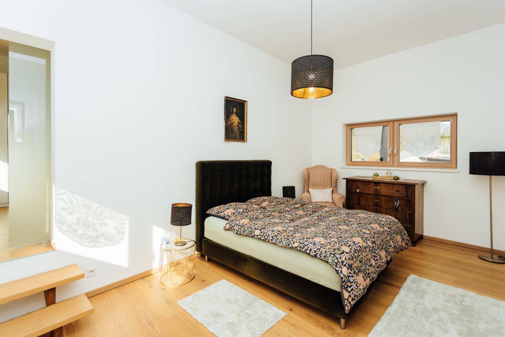 Helles Schlafzimmer mit Parkettboden, Doppelbett und traditioneller Kommode.