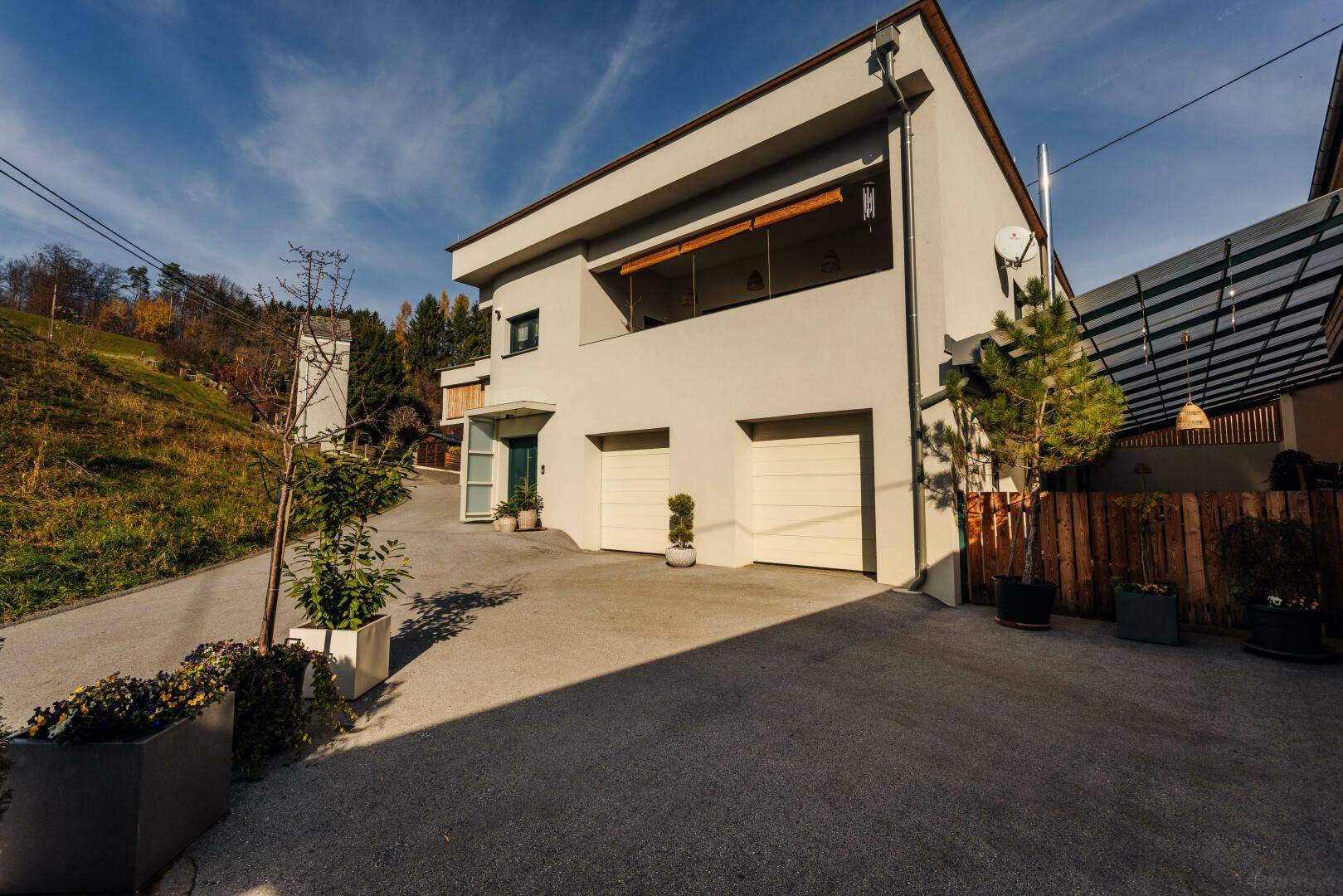 Modernes Wohnhaus mit Garagen, Auffahrt und begrüntem Hang im Hintergrund.
