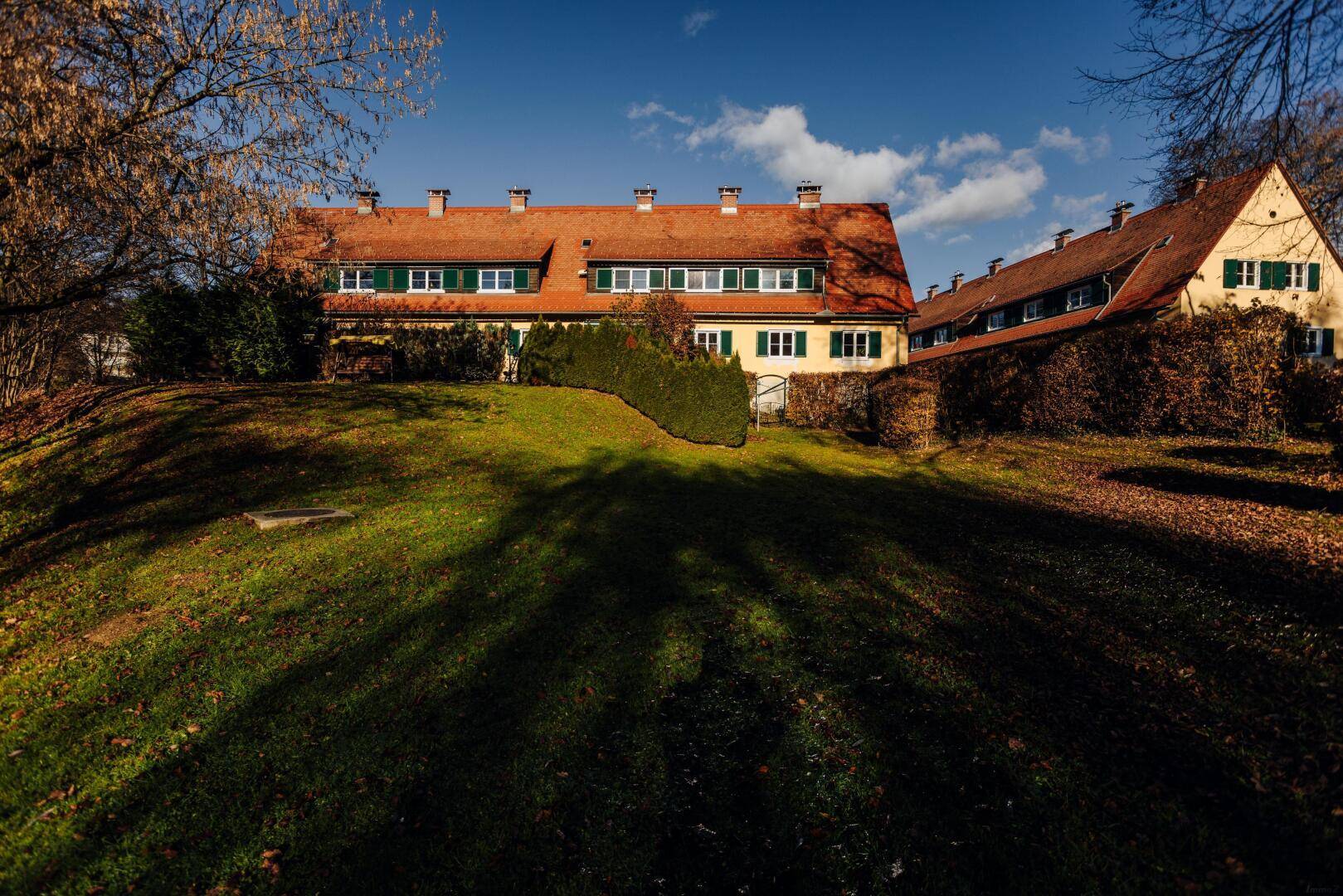 Traditionelle Häuser mit roten Ziegeldächern und grünen Fensterläden, umgeben von gepflegten Rasenflächen.