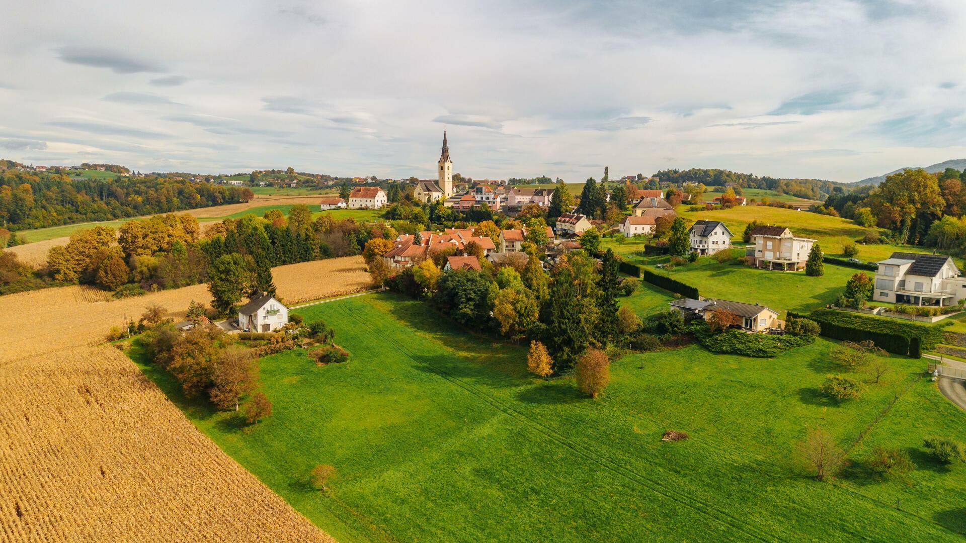 Luftaufnahme eines malerischen Dorfes eingebettet in eine ländliche Herbstlandschaft mit Feldern und Wäldern.