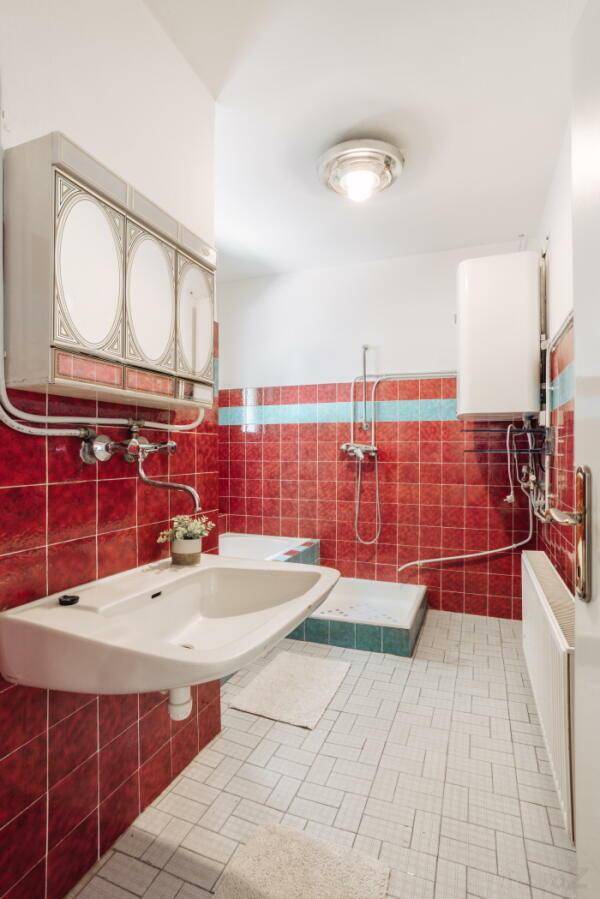 Funktionales Badezimmer mit roten und weißen Fliesen, Waschbecken und Duschbereich.