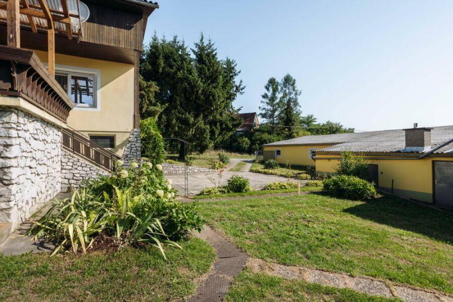 Weitläufiger Garten mit Rasenfläche, Zufahrt und Blick auf das Haus und Nebengebäude.