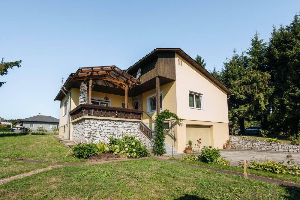 Charmantes Haus mit gelber Fassade, Steinsockel und überdachtem Eingangsbereich, umgeben von Grün.