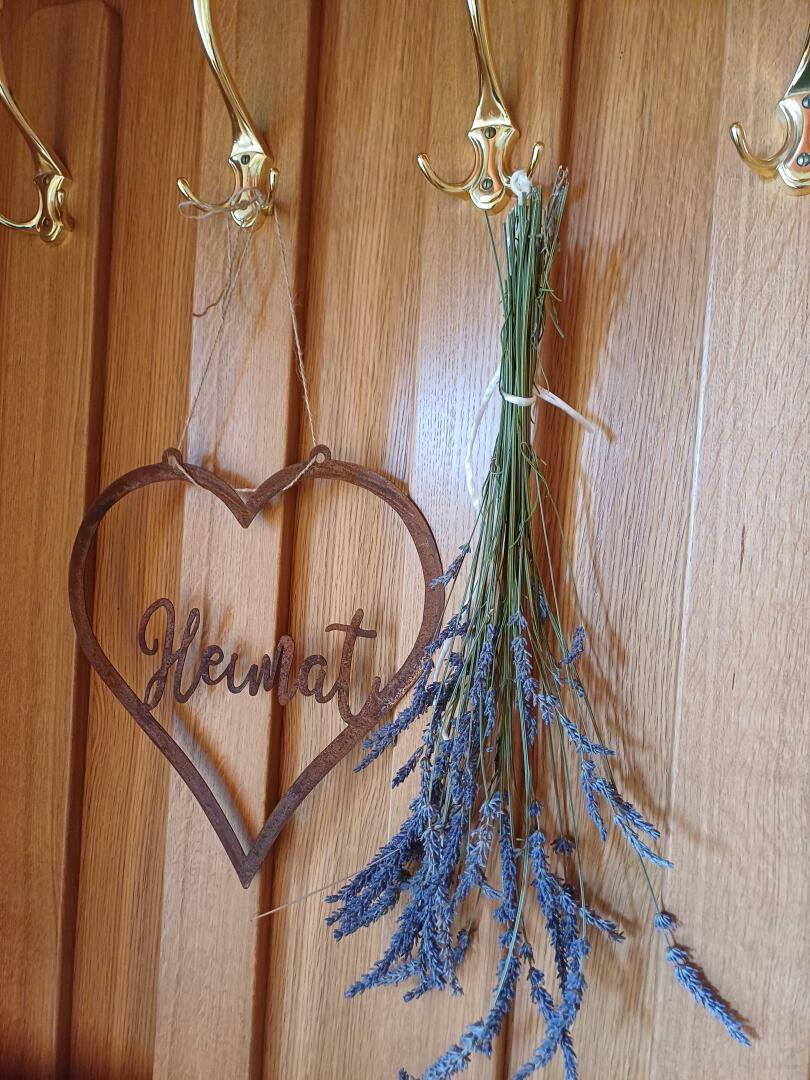 Detailaufnahme einer Holzwand mit Garderobenhaken, einem Herzschild und getrocknetem Lavendel.