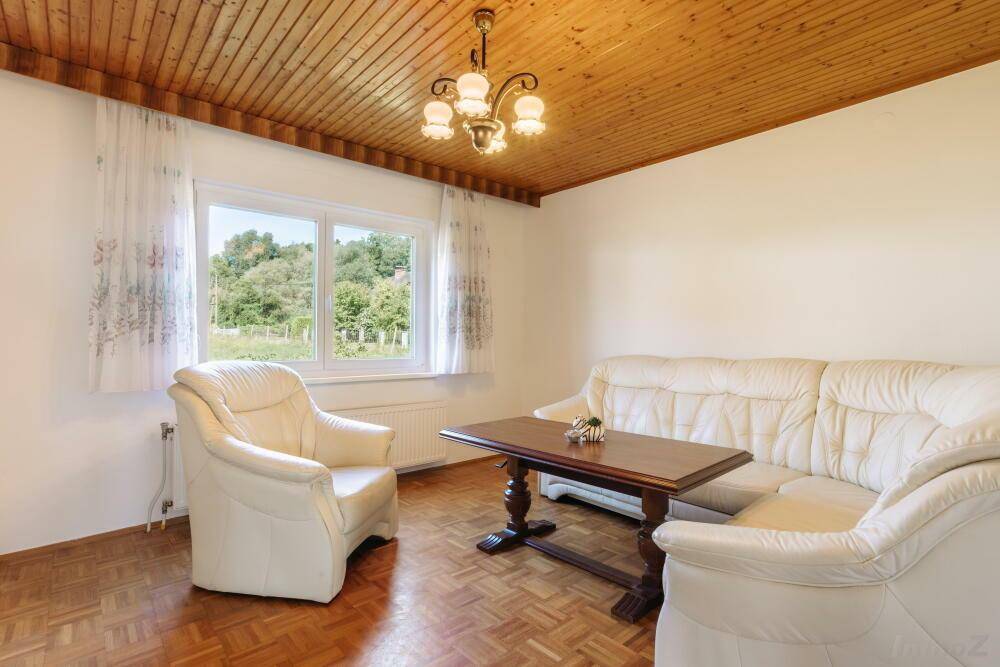 Helles Wohnzimmer mit Holzbalkendecke, Parkettboden und bequemen weißen Ledersofas.