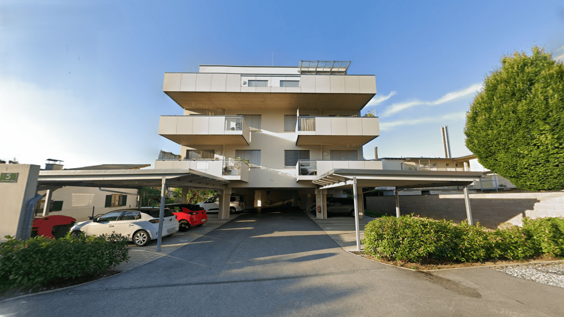Moderne Wohnanlage mit mehreren Carports und gepflegter Außenanlage unter blauem Himmel.