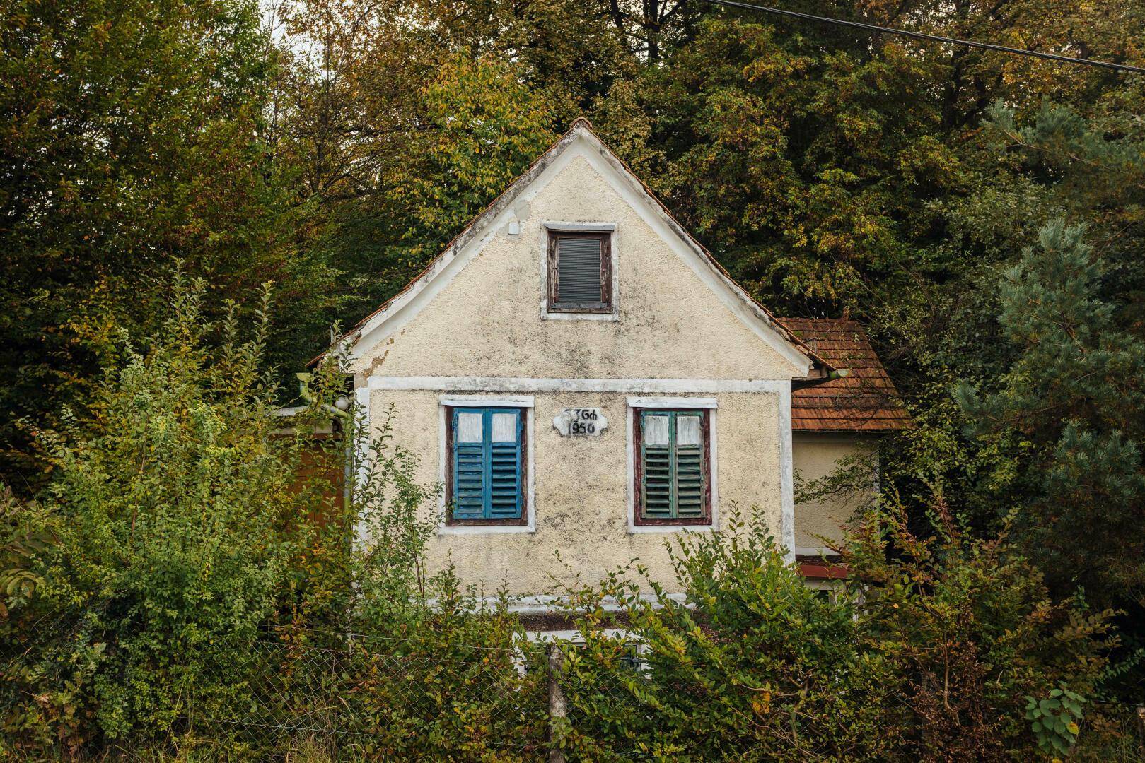 Fassade eines alten Hauses mit verwittertem Putz, kleinen Fenstern und bunten Fensterläden.