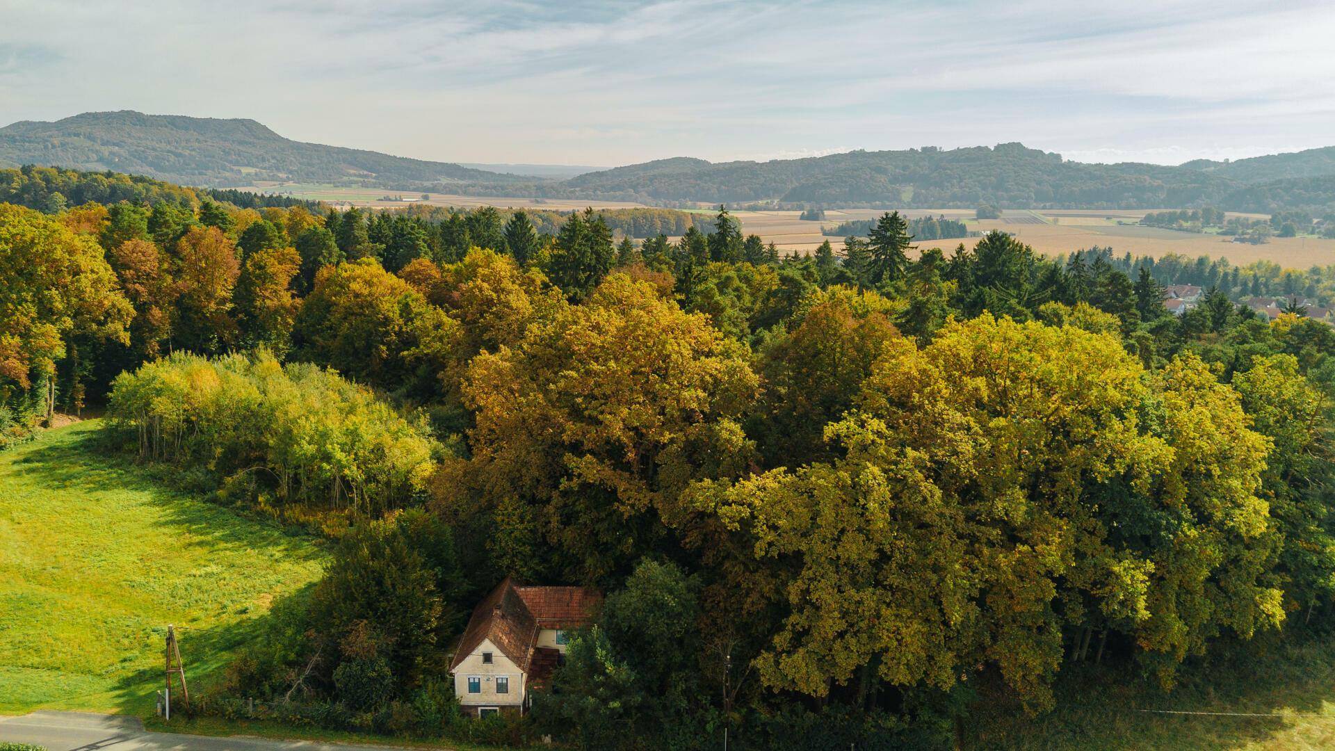 Luftaufnahme eines alten Hauses, umgeben von herbstlichen Bäumen mit weitem Blick auf die Landschaft.