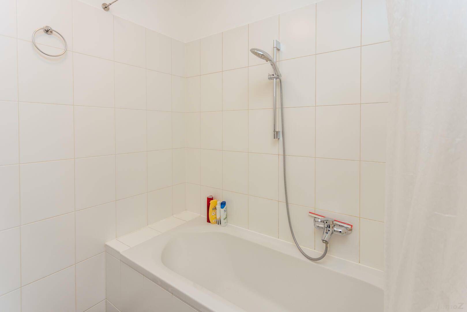 Badezimmer mit Badewanne, Duschvorrichtung und weißen Fliesen.