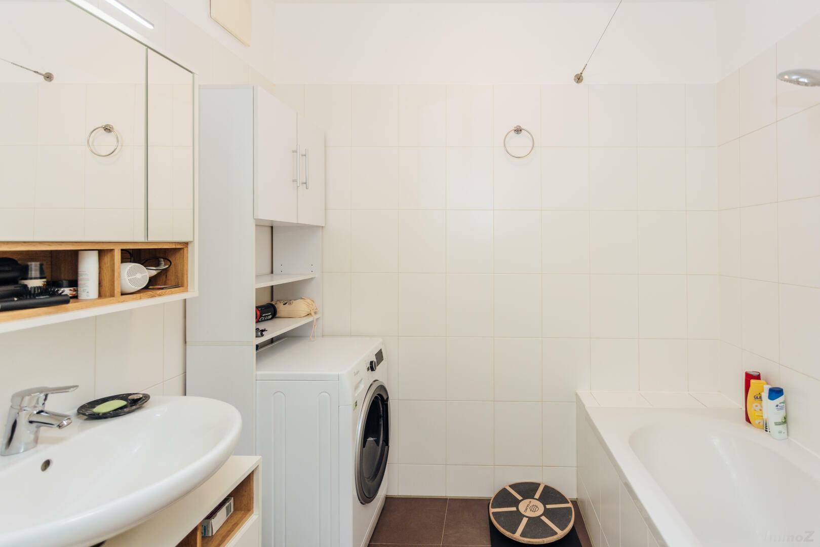 Helles Badezimmer mit Waschbecken, Spiegelschrank und Waschmaschine.