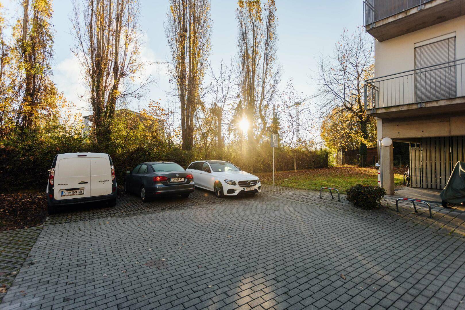 Außenparkplätze vor dem Gebäude mit Bäumen und Sonnenschein im Herbst.
