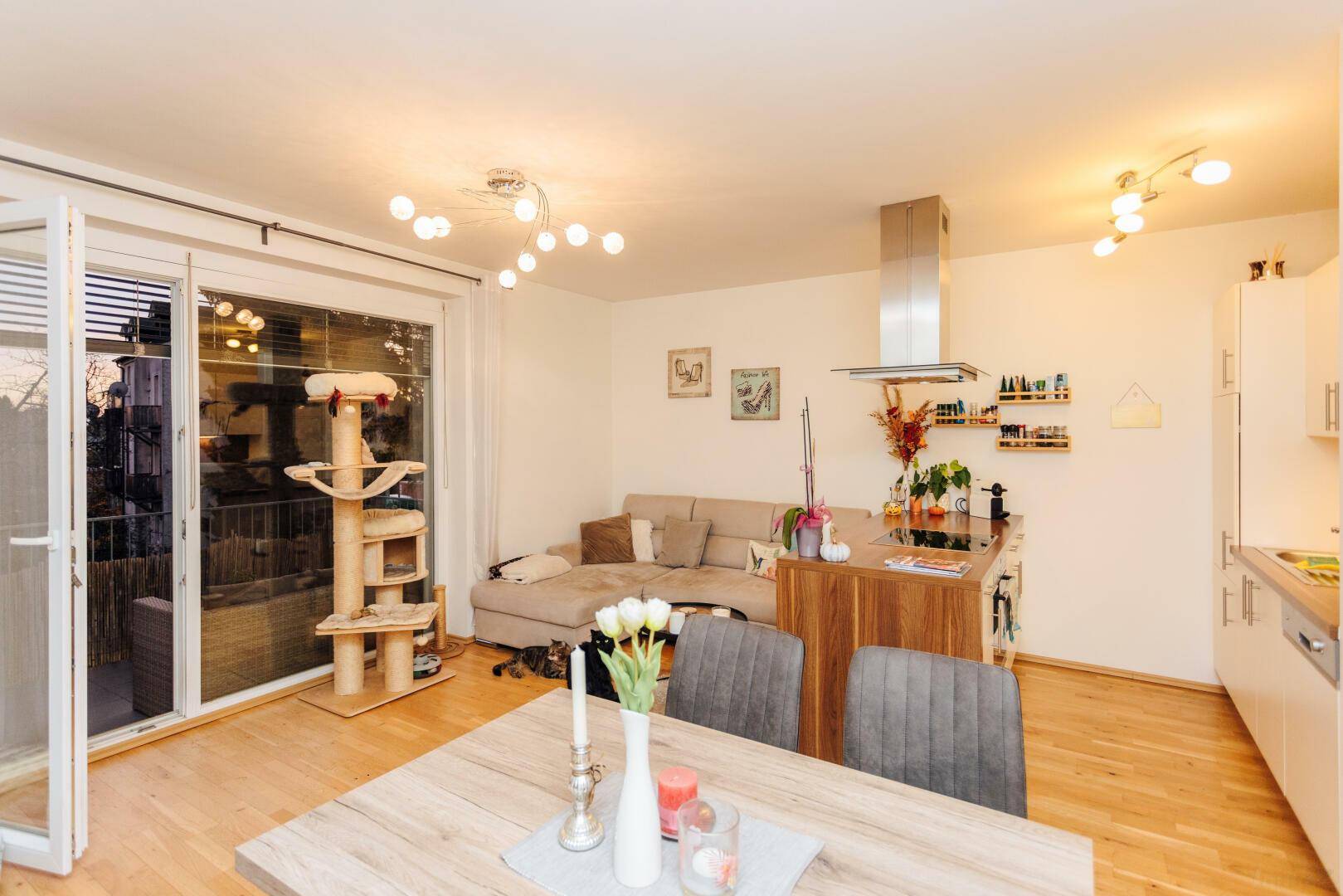 Offener Wohnbereich mit Zugang zum Balkon, Parkettboden und integrierter Küchenzeile.