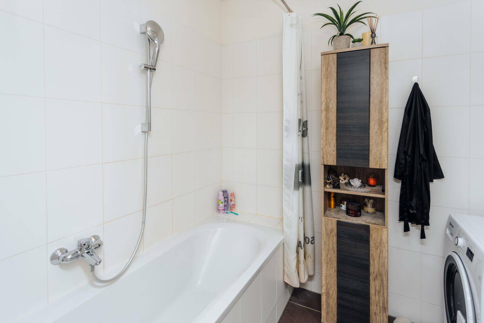 Badezimmer mit Badewanne, Duschvorhang und praktischem Hochschrank.