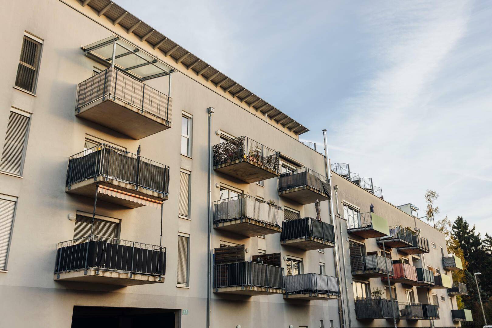 Moderne Wohnhausfassade mit mehreren Balkonen unter einem bewölkten Himmel.