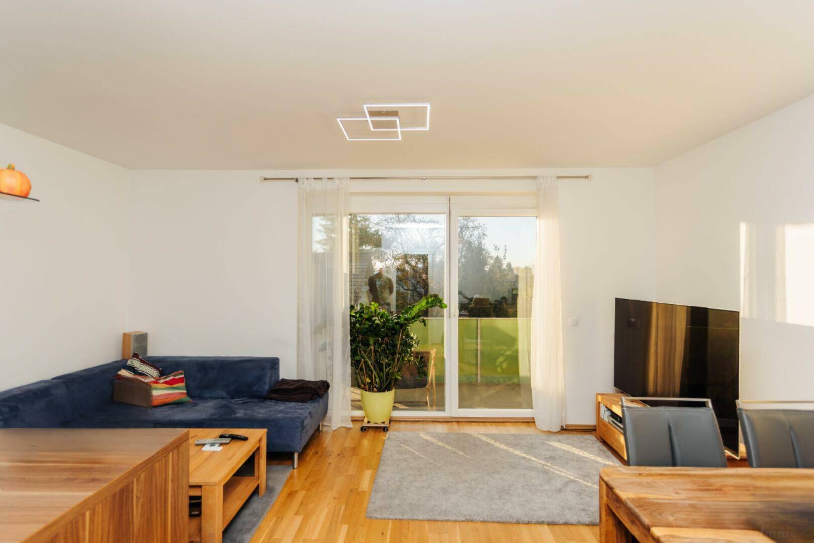 Geräumiger Wohnbereich mit bequemer Couch, Parkettboden und großen Fenstern.