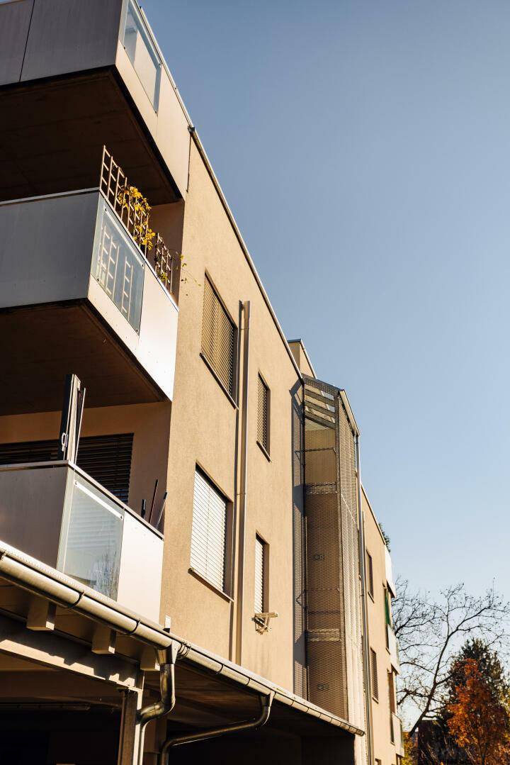 Moderne Gebäudefassade mit Balkonen und Jalousien unter blauem Himmel.