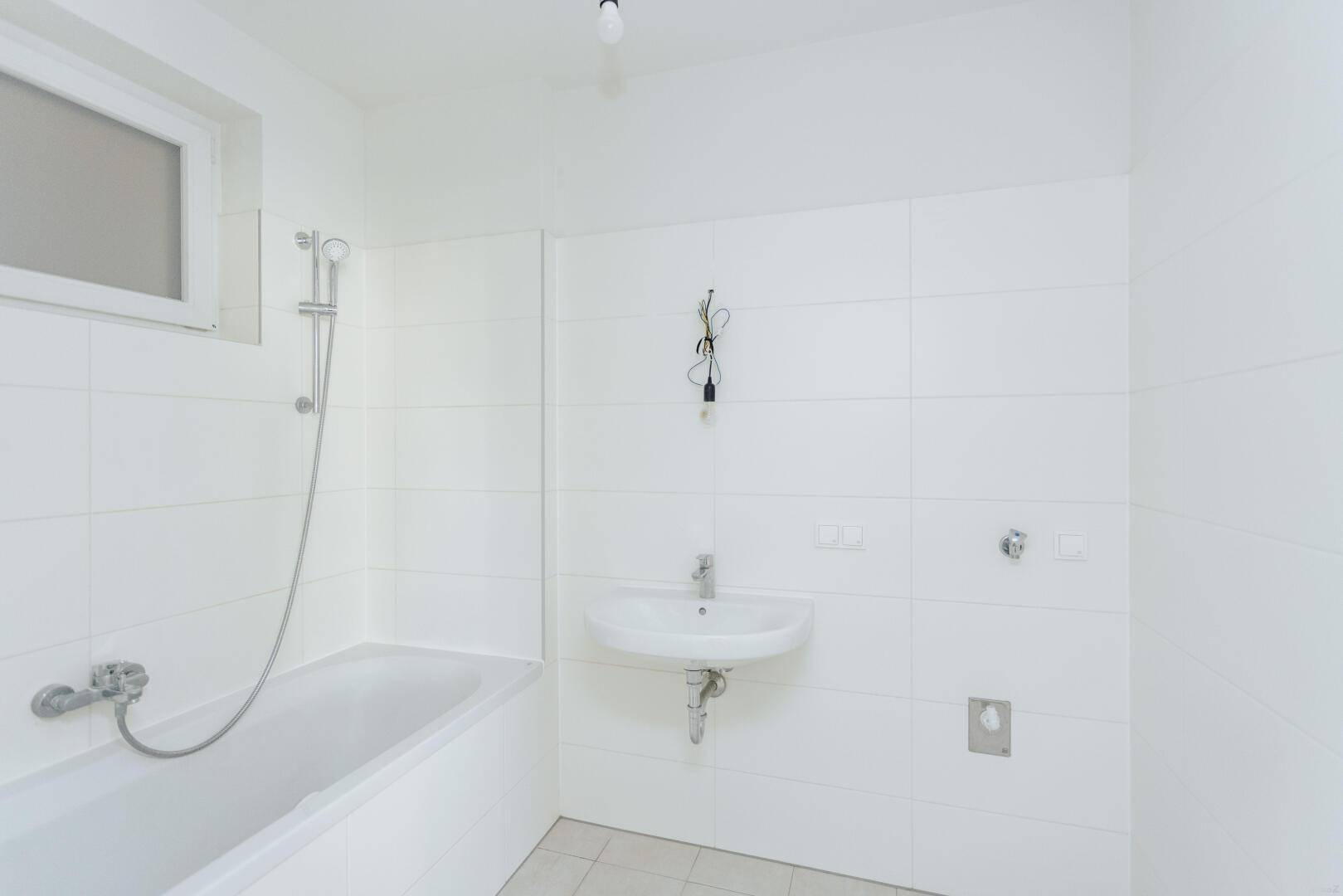 Modernes Badezimmer mit Badewanne, Waschbecken und weißen Fliesen, hell und funktional.