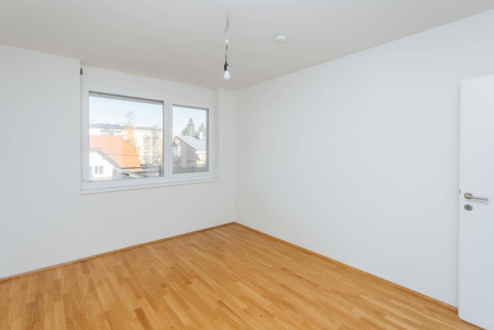 Helles Schlafzimmer mit Parkettboden und großem Fenster, bietet viel Tageslicht.