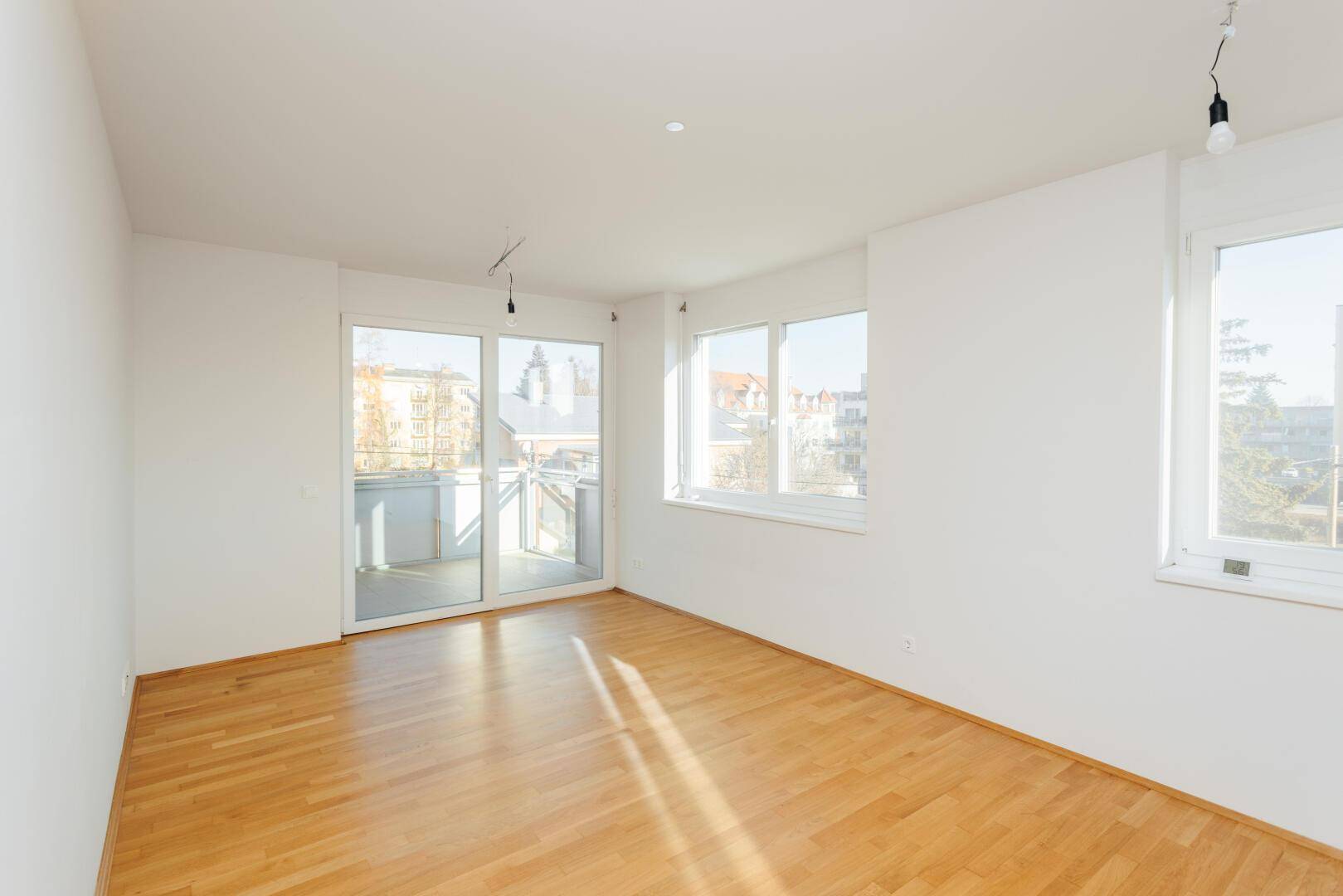Geräumiges Wohnzimmer mit Parkettboden und Zugang zu einem sonnigen Balkon, lichtdurchflutet.