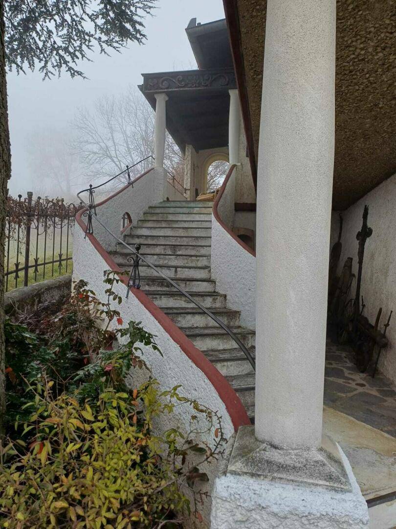 Geschwungene Außentreppe mit schmiedeeisernem Geländer und Säulen, umgeben von Nebel und Bäumen.