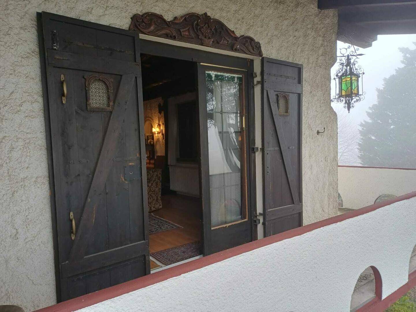 Rustikale Holztüren mit Schnitzereien führen auf einen kleinen Balkon mit schmiedeeiserner Laterne.
