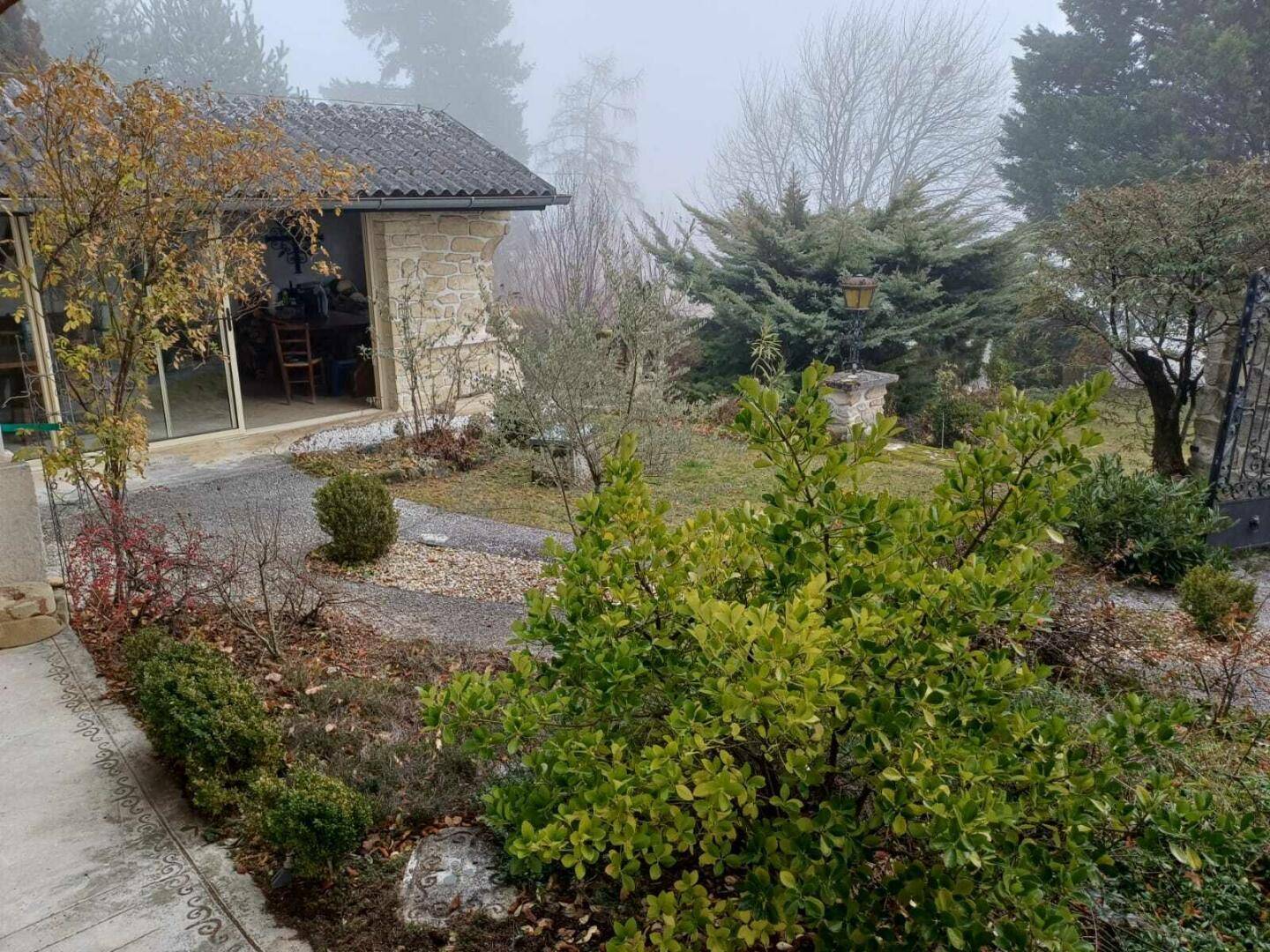 Gepflegter Gartenbereich mit Kieswegen und Sträuchern, angrenzend an ein Nebengebäude mit Glasfront.