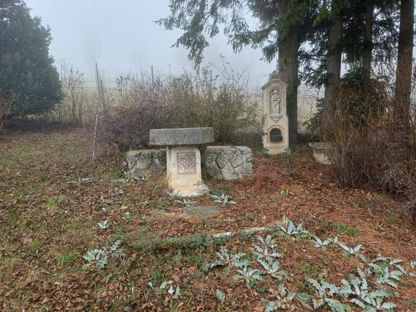 Neblige Außenanlage mit religiösen Statuen und Bäumen in einer ländlichen Umgebung.