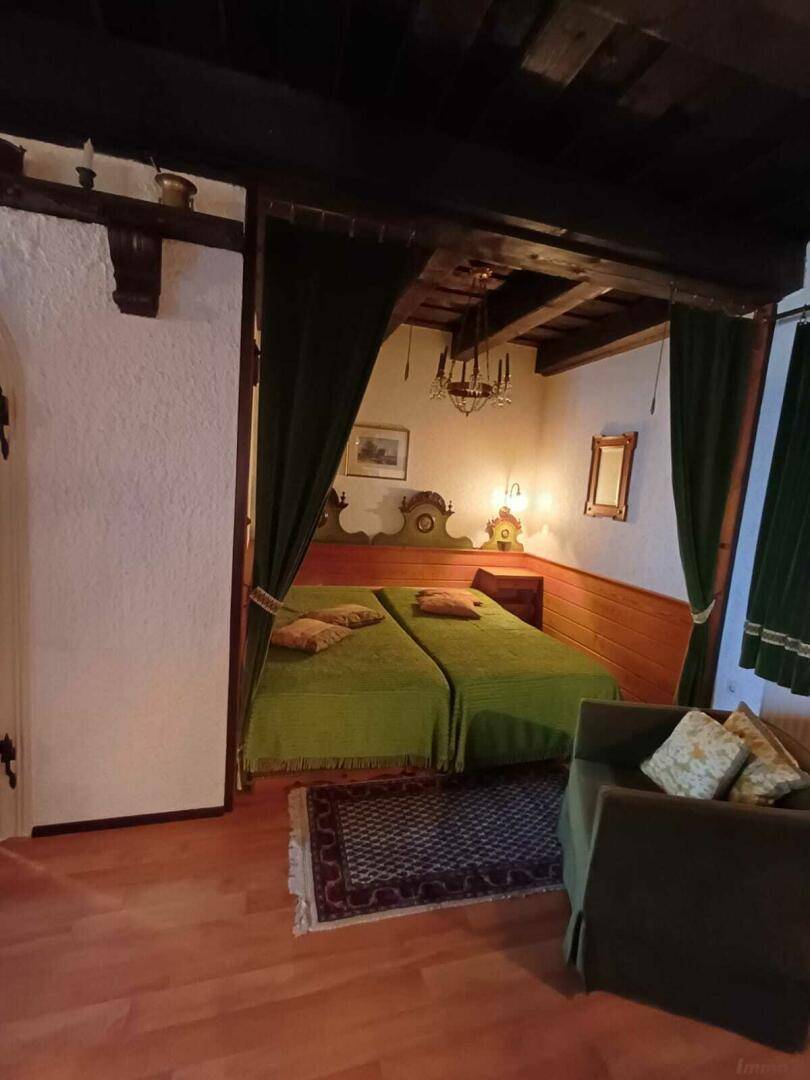 Schlafzimmer mit zwei Einzelbetten, grünen Vorhängen und sichtbaren Holzbalken an der Decke.
