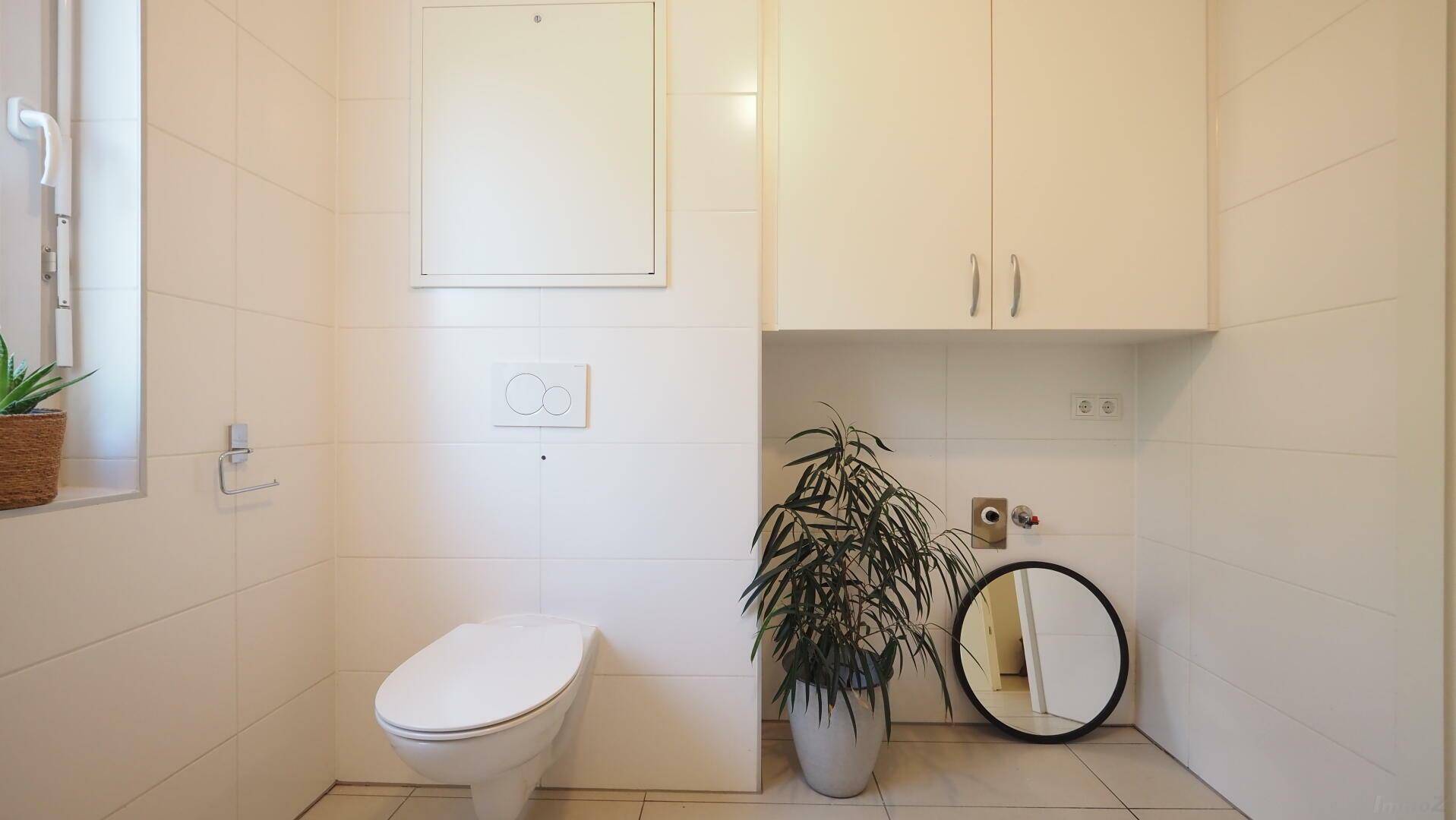 Modern gefliestes WC mit wandhängender Toilette und praktischen Oberschränken.