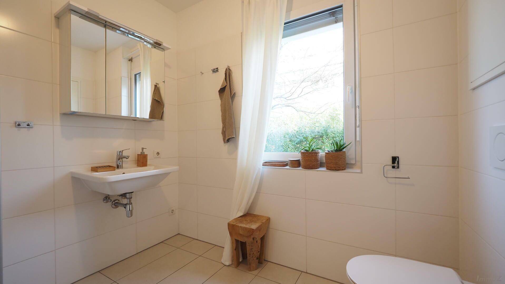 Helles Badezimmer mit Fenster, modernem Waschbecken und Spiegelschrank.