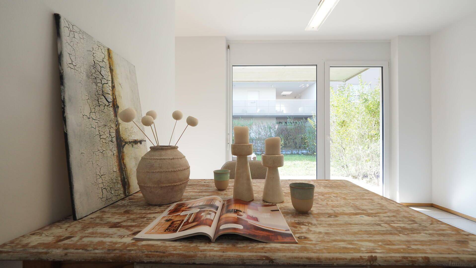 Rustikaler Esstisch mit Dekoration und großem Fenster mit Blick auf den Garten.