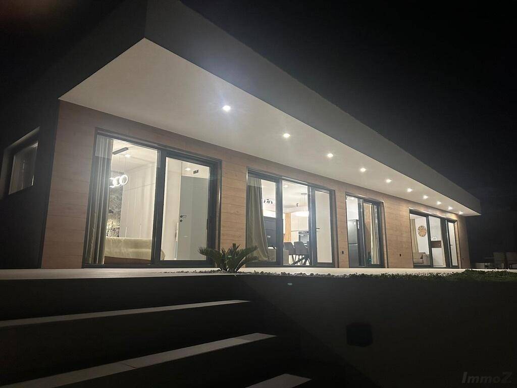 Moderne Villa bei Nacht mit beleuchteter Fassade und angrenzender Terrasse.
