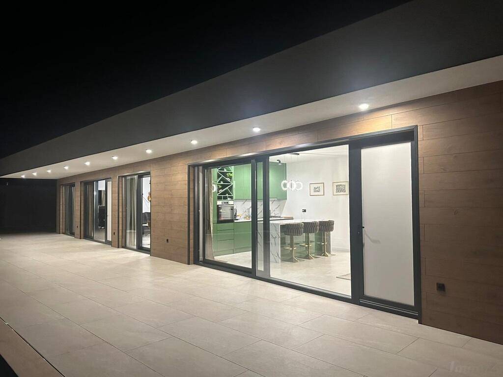 Beleuchtete moderne Hausfassade mit großen Glasfronten und Terrasse bei Nacht.