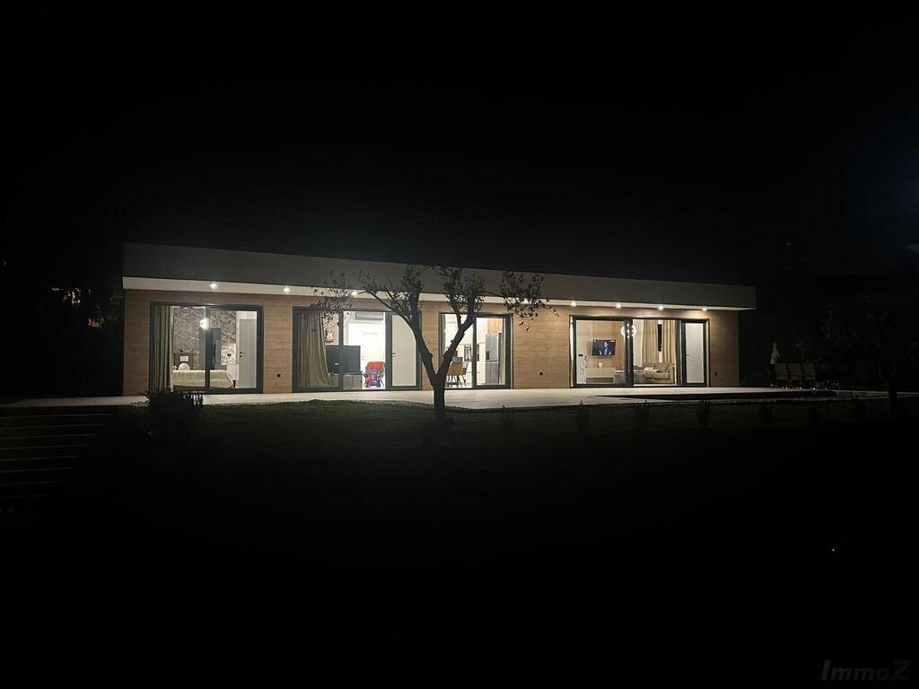 Moderne Hausfassade bei Nacht mit beleuchteten Innenräumen und Garten.